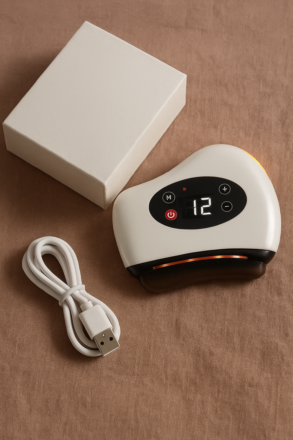 The white heated gua sha on linen beside a plain white box and a coiled white USB charging cable.